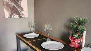 Een eetruimte met een tafel gedekt voor twee personen, twee wijnglazen en een kleine kerstboom.