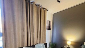 Een kamer met een zwarte bank, een bed, een nachtkastje met lamp en een wandlamp.