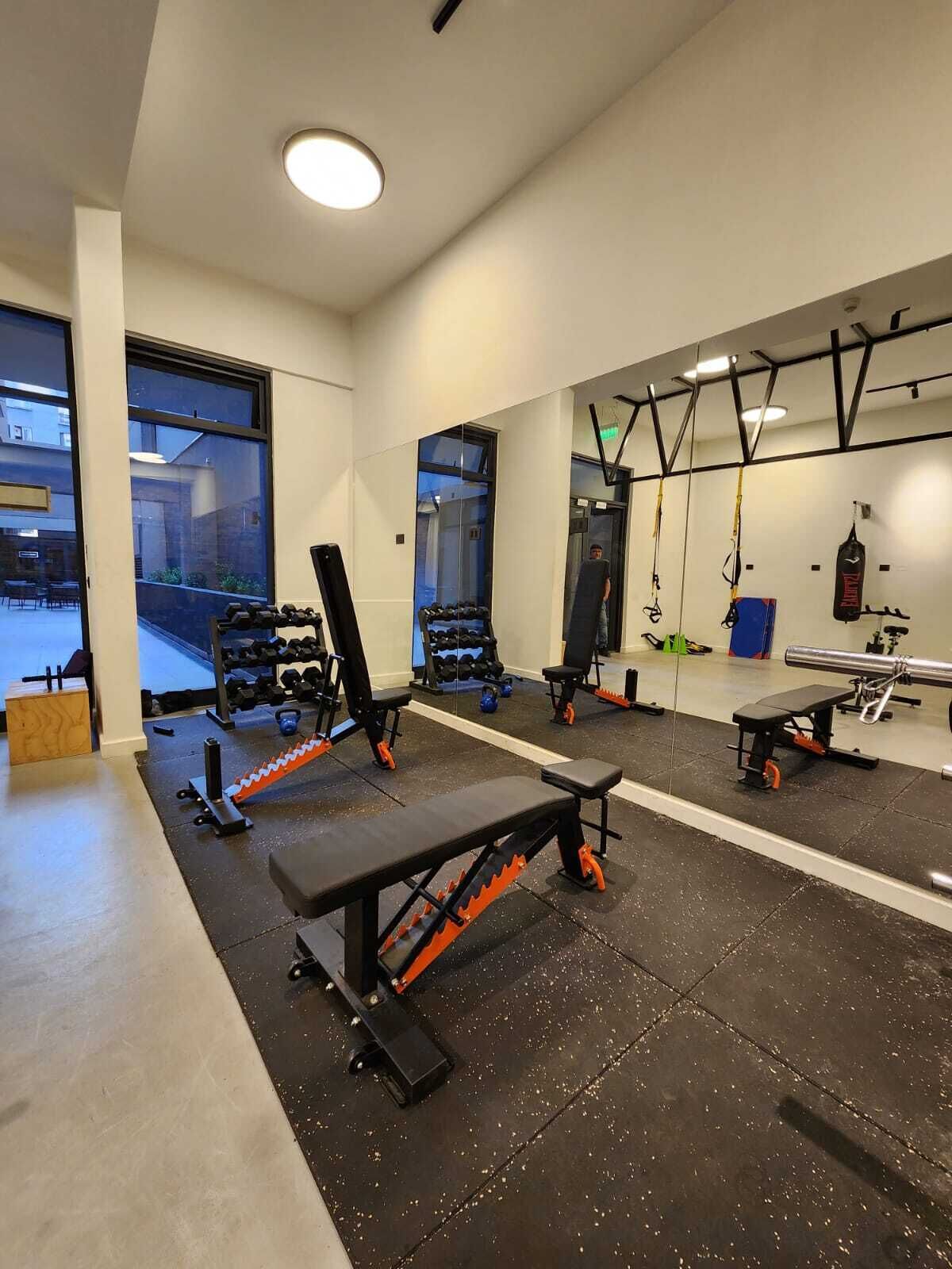 Un gimnasio con equipo de levantamiento de pesas, bancos y un saco de boxeo.