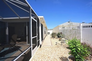 Un bâtiment moderne doté de grandes portes vitrées, d’un patio avec des chaises et d’un chemin de gravier menant à une clôture blanche.