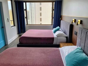 Ein Hotelzimmer mit zwei Betten, einem Fenster mit Vorhängen, Blick auf Gebäude und einer Wandleuchte.