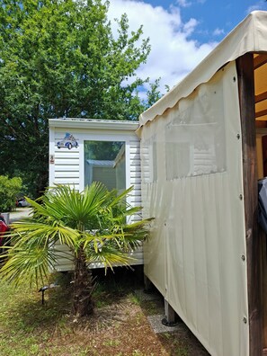 A mobile home with a window, a palm tree, and a vehicle parked nearby. - Lovely mobile home carcans in 3-star campsite (Carcans)