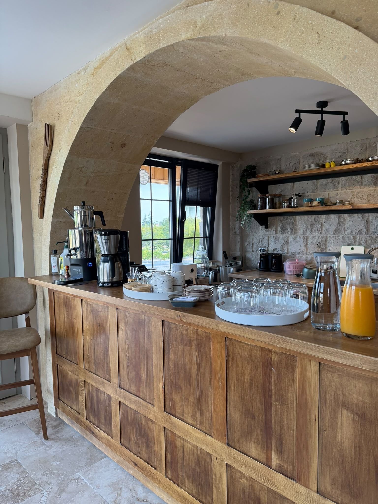 A kitchen with a wooden bar, coffee machines, and various kitchenware.