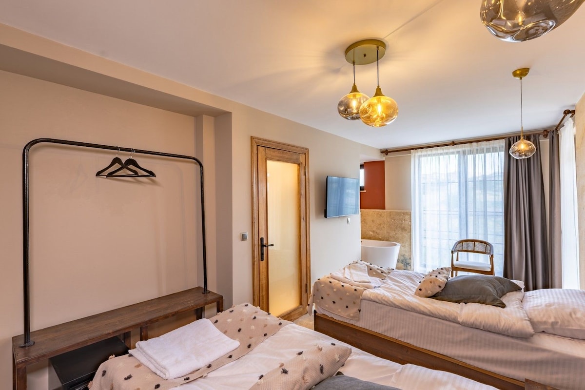 Una habitación de hotel con dos camas, televisión, baño y ventana con cortinas.