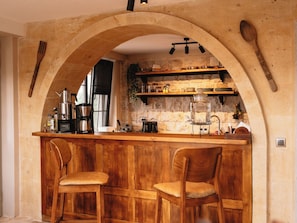 Eine rustikale Küche mit einer gewölbten Steinwand, Holzbarhocker und einer Kaffeemaschine.