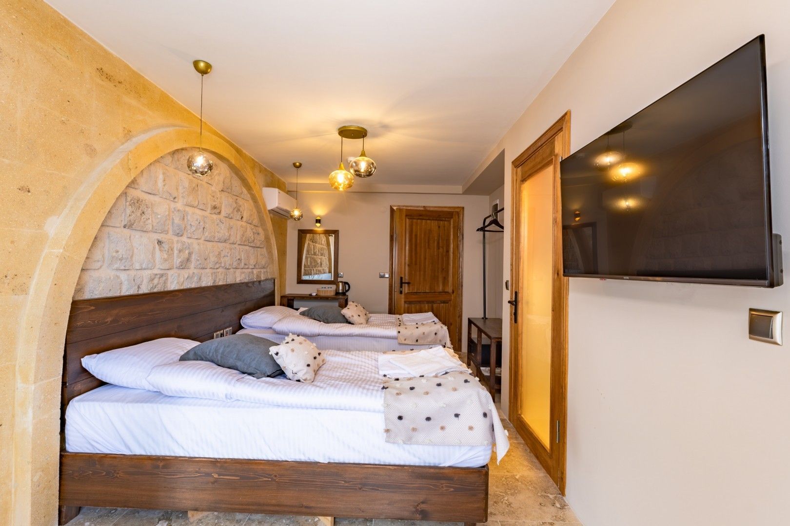 Een slaapkamer met een stenen boog, een houten bed, een flatscreen televisie en een klein tafeltje.