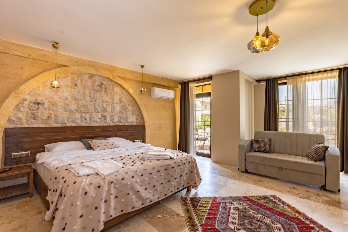 Un dormitorio con pared de arco de piedra, una cama con colcha estampada, un sofá y un ventanal con cortinas.