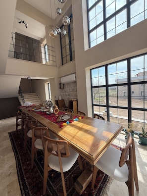 Un comedor amplio con techo alto, ventanas grandes y una escalera que sube a un nivel superior.