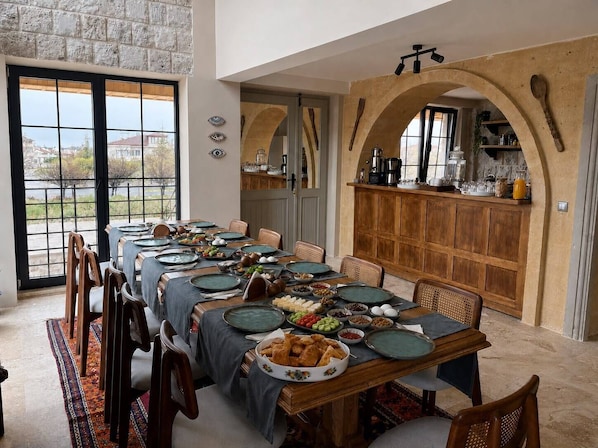 Comedor con una mesa larga dispuesta para una comida, cocina con armarios de madera y vistas a través de amplios ventanales.