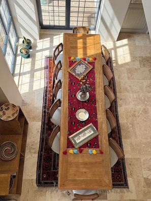 Un comedor con una mesa de madera, sillas, un mantel decorado y vistas a través de amplios ventanales.