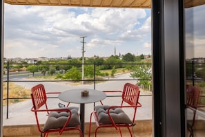 Ein Balkon mit zwei roten Stühlen und einem kleinen Tisch, mit Blick auf eine Straße und Grünflächen.