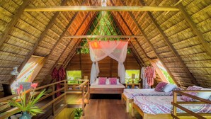 Une chambre mansardée avec un plancher en bois, un lit à baldaquin, un bureau avec un ordinateur et une fenêtre donnant sur un paysage verdoyant.