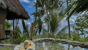 Un complexe hôtelier tropical doté de bungalows aux toits de chaume, d’une fontaine en pierre et d’une végétation luxuriante.
