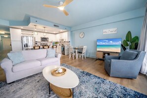 Ein modernes Wohnzimmer mit einer Couch, einem Sessel und einem Couchtisch. Im Hintergrund befindet sich ein Essbereich mit Tisch und Stühlen sowie eine Küche.