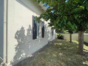 A building with white exterior walls, a small garden area with grass, and a tree. - Large family home 🌿 Garden, terrace & ocean 10 min away (Biscarrosse)