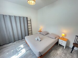 A bedroom with a bed, two bedside tables with lamps, a chair, a ladder, and a window with curtains. - Large family home 🌿 Garden, terrace & ocean 10 min away (Biscarrosse)