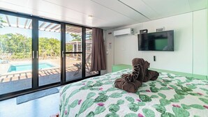 Et hotelværelse med seng, fjernsyn, vindue med udsigt til pool og grønne områder, samt en aircondition.