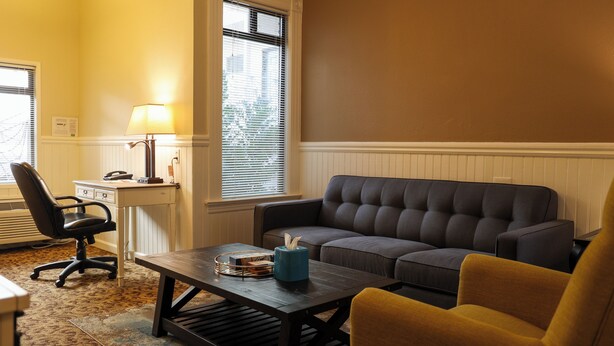 Una sala de estar con sofá, sillón, mesa de centro, lámpara y un escritorio con silla.
