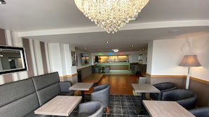 A hotel lobby with seating areas, a chandelier, a reception desk, and a visible kitchen area. - The Strand Hotel (Blackpool)