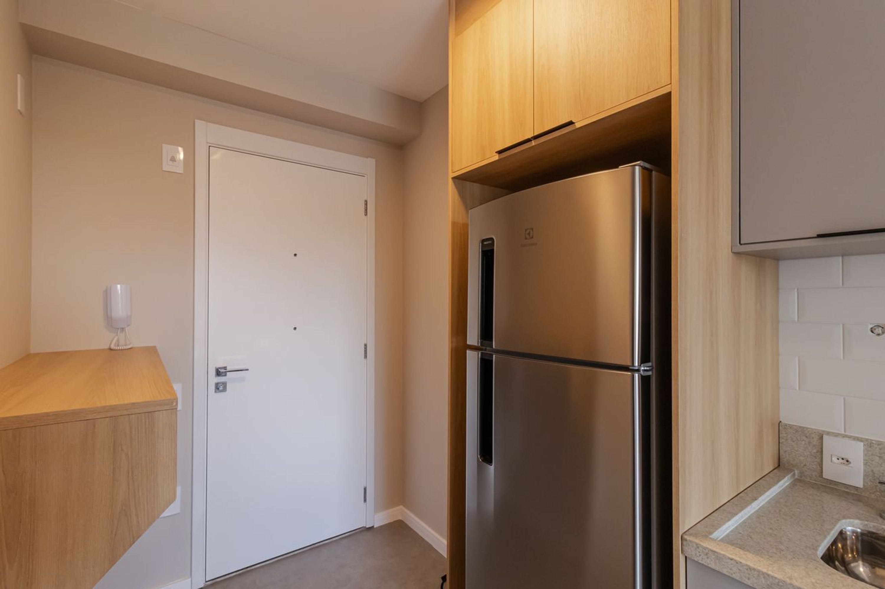 Een kleine keuken met een koelkast van roestvrij staal, houten kastjes en een witte deur.