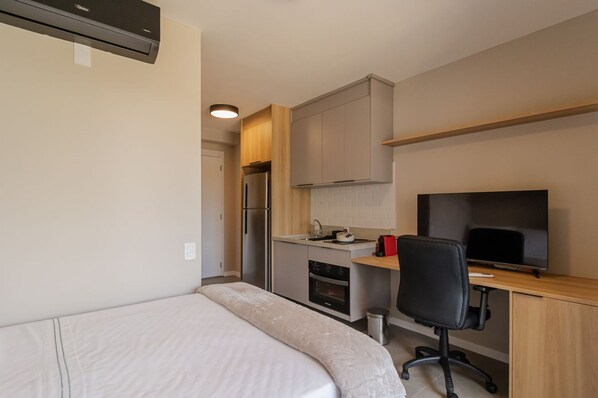 A compact hotel room with a bed, kitchenette, TV, and a desk. - Studio c Academia Perto do Aeroporto de Congonha (São Paulo)