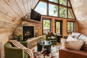 Ein gemütliches Blockhaus-Interieur mit Kamin aus Naturstein, Holzwänden, einer Ledersofa und einem an der Wand befestigten Fernseher.