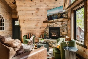 Ein gemütliches Blockhaus-Interieur mit Kamin aus Stein, Ledersofa und einem darüber montierten Fernseher.