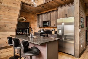 Eine Küche mit Holzwänden, einem Edelstahl-Kühlschrank, einer Mikrowelle und einer Bar mit Hockern.