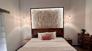 A bedroom with a large bed, a headboard with a textured design, two bedside lamps, a wooden nightstand, a small table with cups, and a chair. - Cozy suite in downtown Morelia (Morelia)