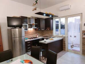 A modern kitchen with a built-in stove, refrigerator, and a dining area with a table and chairs. - Casa Vacanze Marylu' a Torre Specchia (Melendugno)