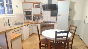 A kitchen with a stove, microwave, sink, and a dining table with chairs. - Large gîte sleeps 14 - 6 ha - ideal for families & cousins - near La Flèche (La Chapelle-d'Aligné)