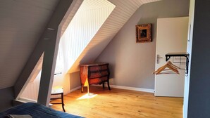 A bedroom with a sloped ceiling, a bed with a blue quilt, a wooden dresser, a hanging rack, and a framed picture on the wall. - Large gîte sleeps 14 - 6 ha - ideal for families & cousins - near La Flèche (La Chapelle-d'Aligné)