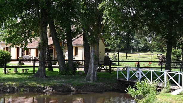 A tranquil riverside setting with a wooden bridge, picnic tables, and a building with a yellow facade. - Large gîte sleeps 14 - 6 ha - ideal for families & cousins - near La Flèche (La Chapelle-d'Aligné)