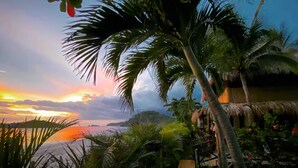 Ein tropisches Resort mit Holzterrasse, Palmen und Blick auf den Ozean bei Sonnenuntergang.