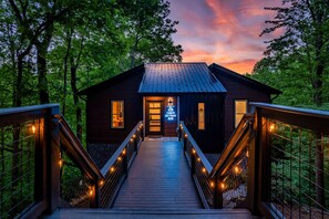 Eine Holzhütte mit einer hölzernen Terrasse, die zum Eingang führt, umgeben von Bäumen.