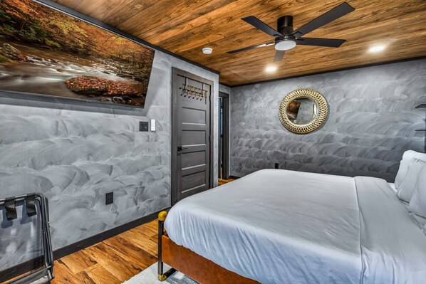 A bedroom with a bed, a ceiling fan, a wall-mounted mirror, and a door with a towel rack. - Cozy 2-bedroom cabin/Amazing Views/Movie Theatre (Gatlinburg)