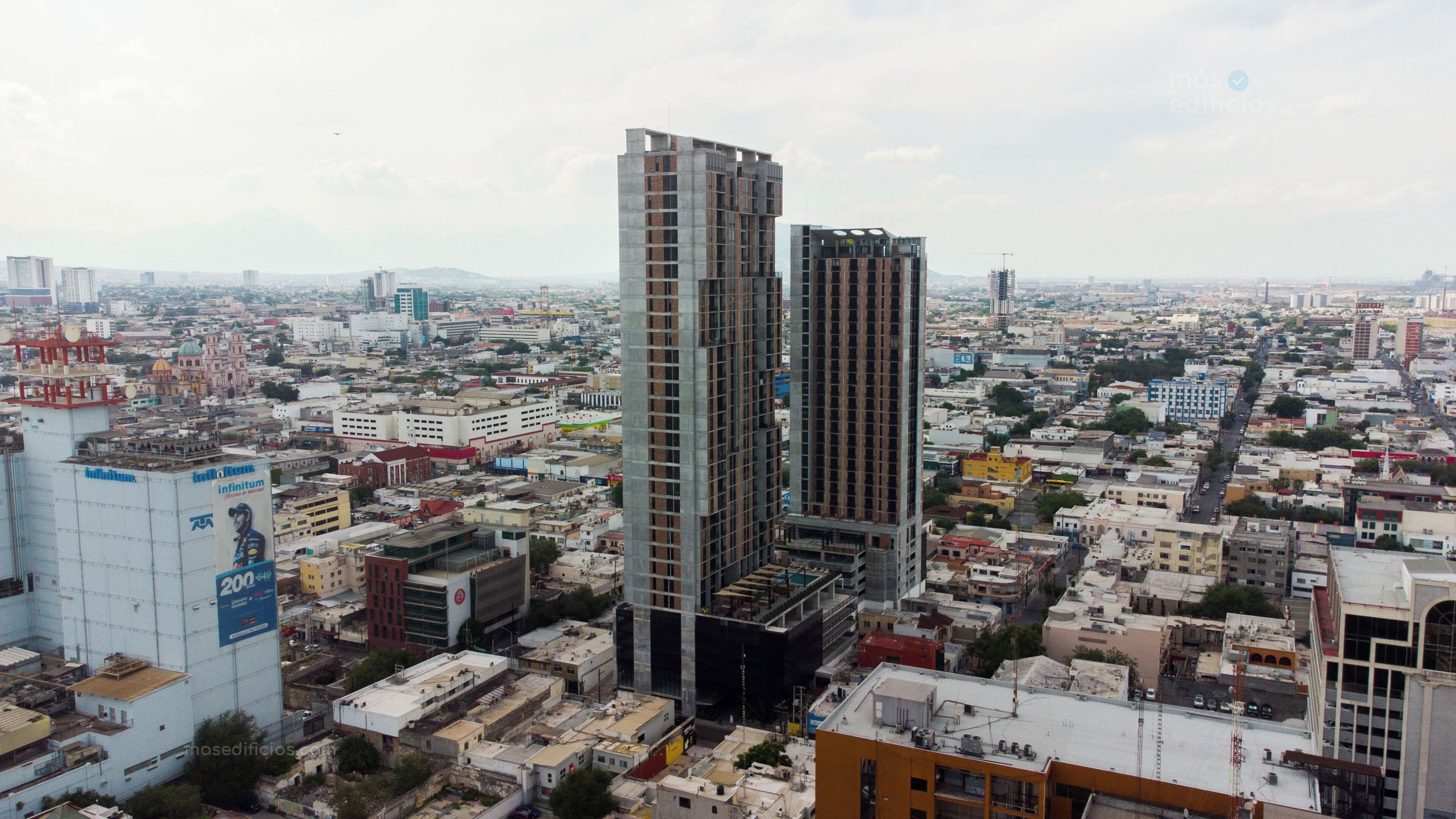 Un immeuble de grande hauteur à l’architecture moderne, situé au cœur d’un quartier urbain dense, entouré d’autres bâtiments de différents types.