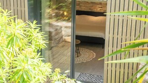 A modern room with a glass door leading to a bed, a small stool, and a patterned rug. - Grande longère entre campagne et océan (Guidel)