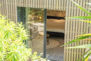 A modern room with a glass door leading to a bed, a small stool, and a patterned rug. - Grande longère entre campagne et océan (Guidel)
