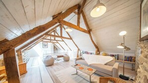 A loft-style room with exposed wooden beams, a white sofa, a wicker chair, a coffee table, and a floor lamp. - Grande longère entre campagne et océan (Guidel)