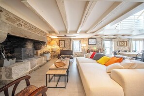 A cozy living room with a fireplace, a sofa with colorful cushions, and a dining area with a table and chairs. - Grande longère entre campagne et océan (Guidel)