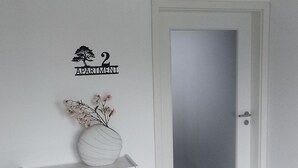 Una porta bianca con un pannello in vetro satinato, uno scaffale con un vaso di fiori e un cartello che indica '2 APARTMENT' appeso al muro.