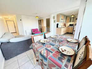Ein Essbereich mit Tisch für vier Personen, einer Couch und einer Küche im Hintergrund.