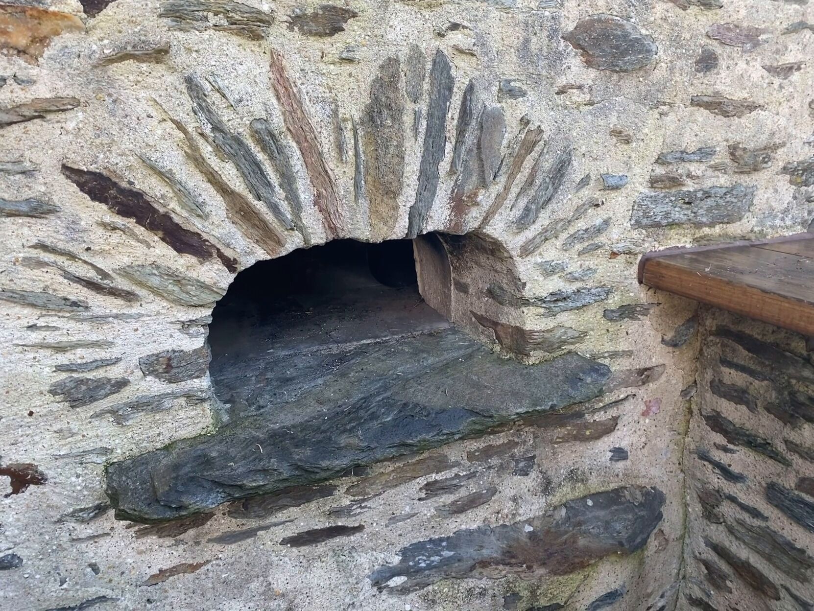 A stone oven with a dark interior and a wooden ledge.