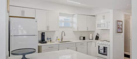 A modern kitchen with white cabinetry, a central island, a built-in oven, and a microwave.