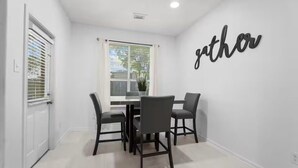 Un comedor con una mesa y sillas, una ventana con persianas, y una pared con la palabra 'gather' escrita.