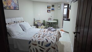 A room with a bed, a small round table, a chair, and a kitchenette. - Cabo Branco apartment in João Pessoa, 180 meters from the beach. (JOAO PESSOA)