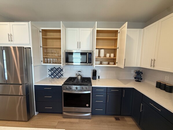 A modern kitchen with white cabinets, a stainless steel refrigerator, a microwave, a stove, and a kettle.