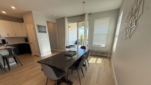 A modern kitchen with a central island, dining area with chairs, and a view through the glass door. - Single Story Ranch l New Build l RMNP l 3bd 2bath l Game room (Loveland)