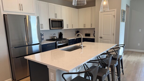 A modern kitchen with stainless steel appliances, a central island with bar stools, and pendant lighting. - Single Story Ranch l New Build l RMNP l 3bd 2bath l Game room (Loveland)